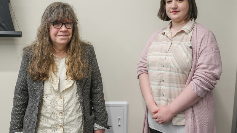 Two women stand in front of a wall in a conference room.