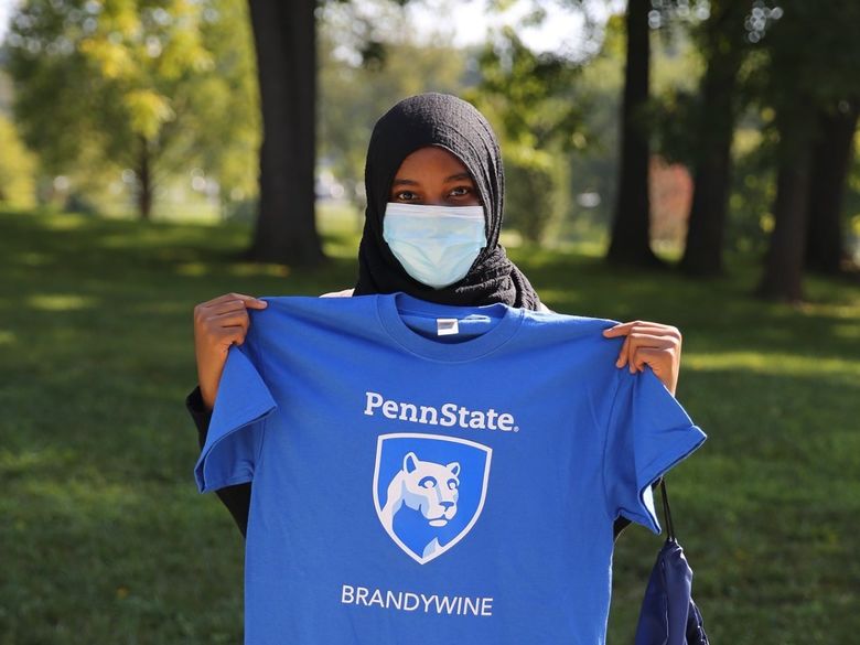 Female student wearing mask and holding up Penn State Brandywine tee shirt.