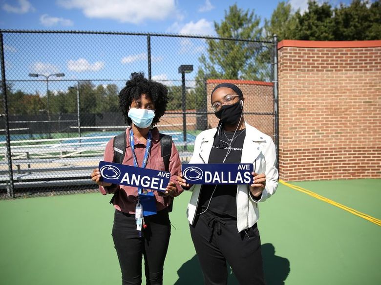 Two female students wearing masks and holding signs with their names.