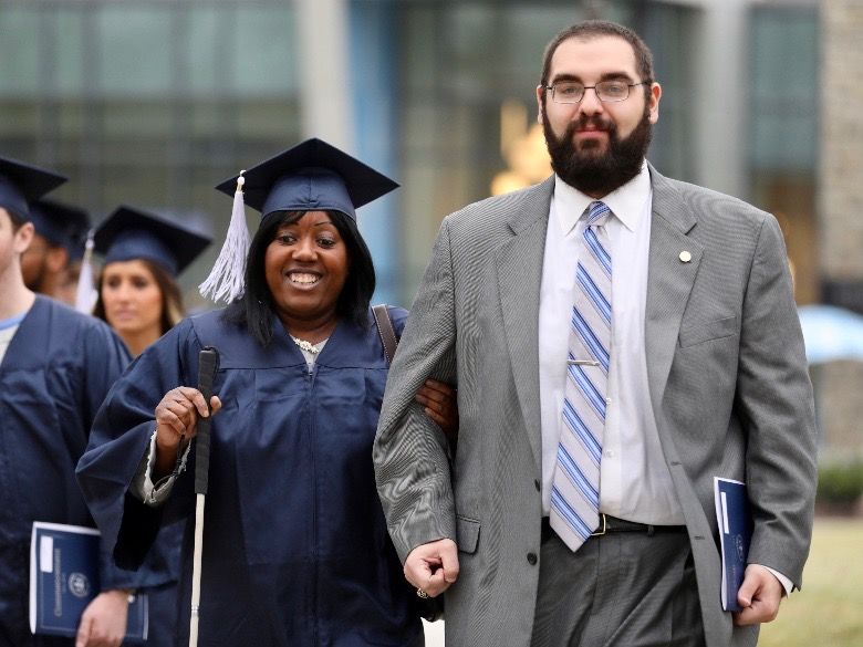 Female student walking to Commencement ceremony with male aid