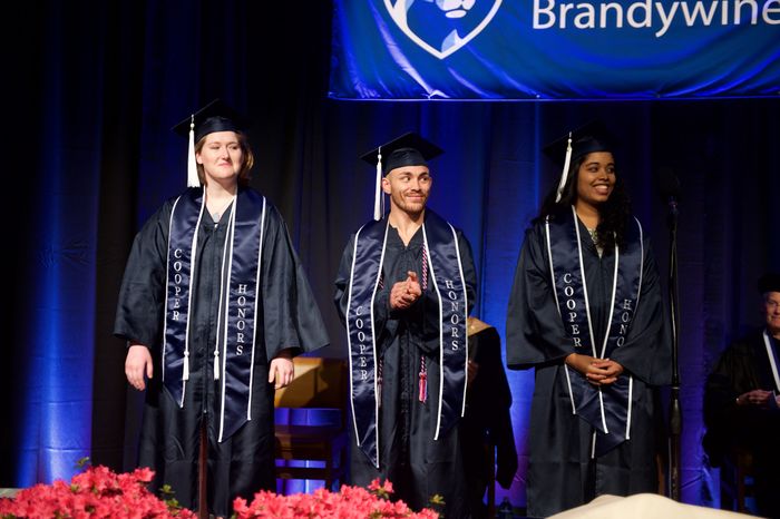 Three students at graduation stand on stage in academic regalia