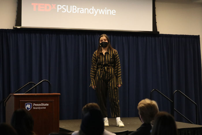 A female student stands on a stage speaking to an audience.