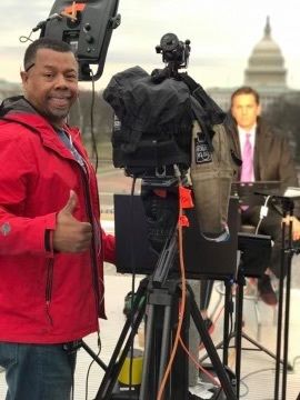 Man with thumb up behind a camera