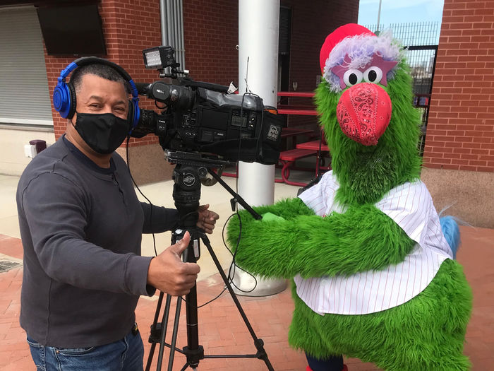 Man with camera wearing mask standing with Philly Phanatic