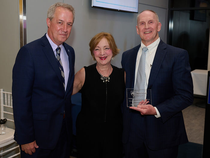 Two men and a woman are standing with one man holding an award.