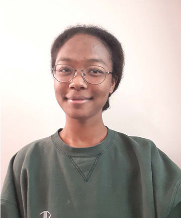 A selfie of Hannah in a green sweatshirt in front of a beige backdrop.