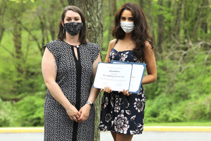 Two women stand outside with one of the women holding award certificates.
