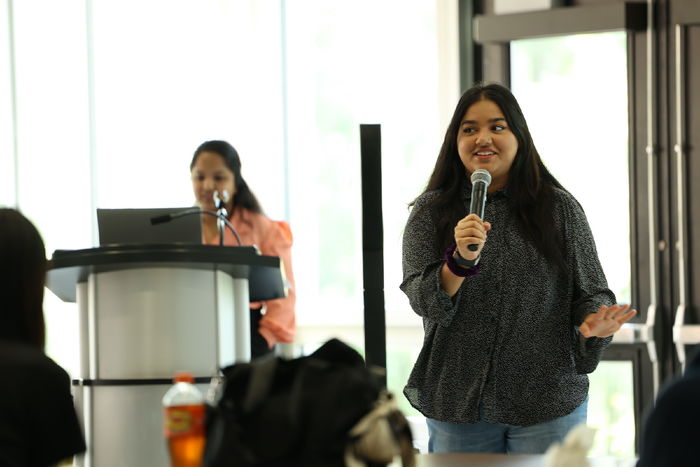 Girl holding a microphone with another girl at a podium