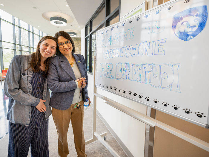 Two women stand next to each other in front of a whiteboard.