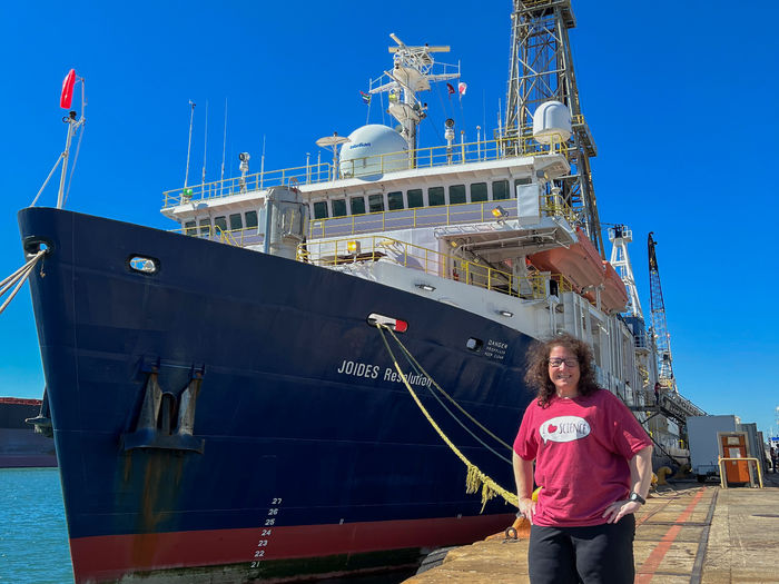 A woman stands on share next to a large ship.