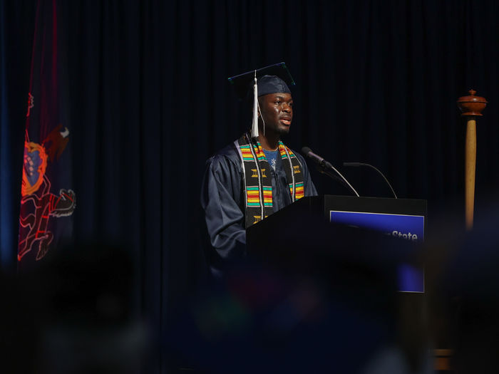 A person wearing a graduation gown speaks at commencement.