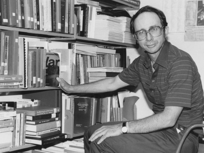 A man sits in an office next to a book shelf.