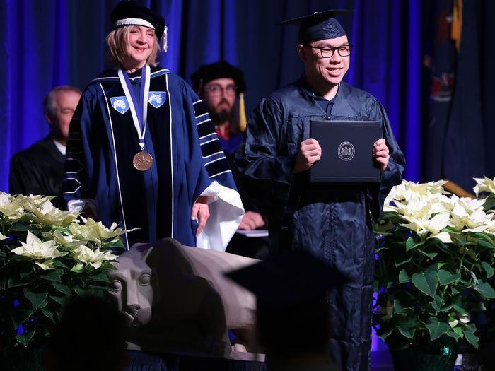 A man stands on a stage holding a diploma cover.
