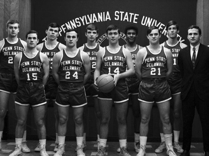 A group of men's basketball players stands in front of a Penn State banner.
