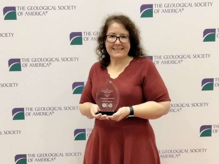 A women holds an award in front of a banner.