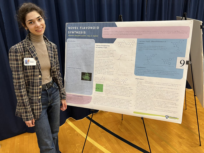 A female student stands next to her poster which is on an easel.