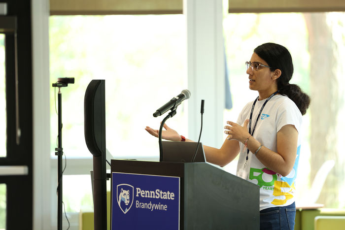 A woman speaks to an audience next to a lectern.