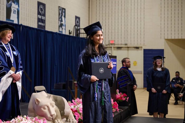 A woman stands on a stage holding a diploma.