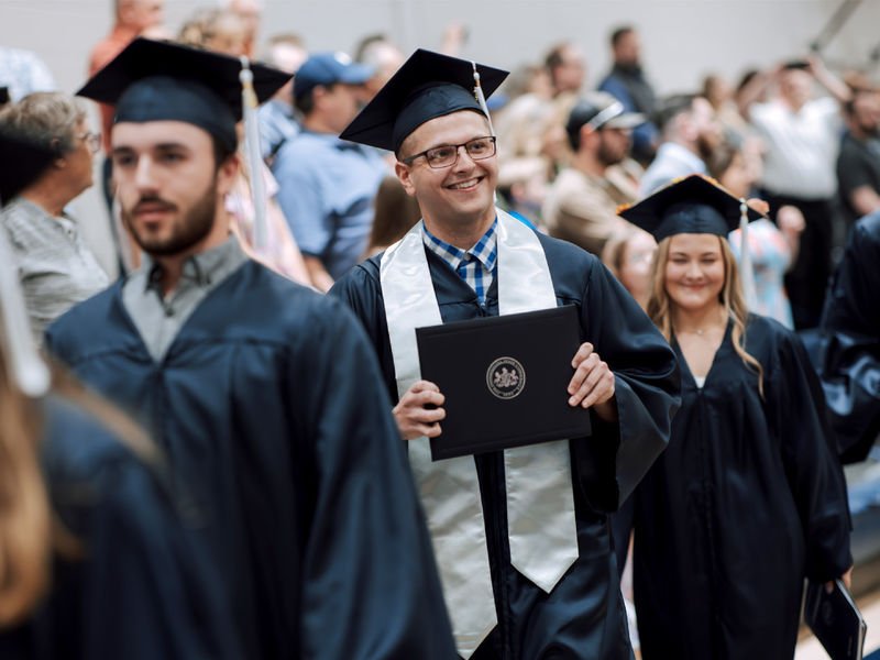 New Penn State graduate Kolton Lyons, who earned an associate degree in business administration, proudly displays his degree to onlooking family and friends during the commencement ceremony at Penn State DuBois.