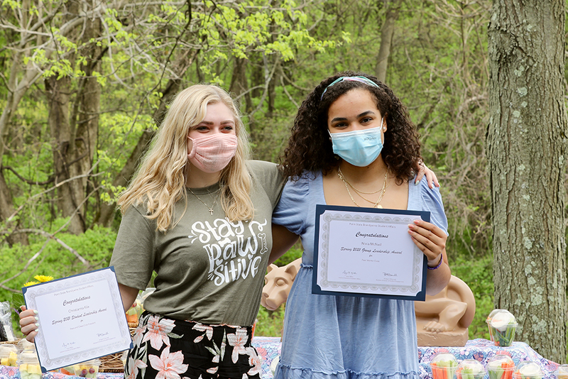 Two female students sharing their award certificates.