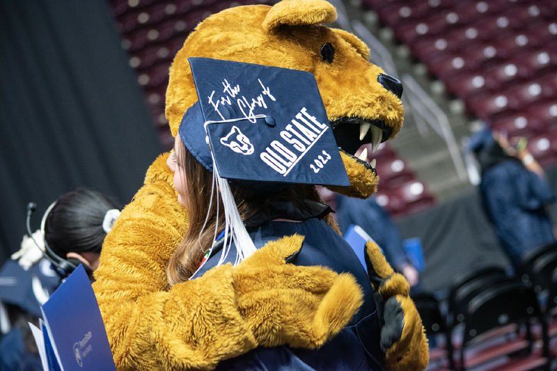 The Nittany Lion hugs a graduate in a cap that reads "For the Glory of Old State 2023"