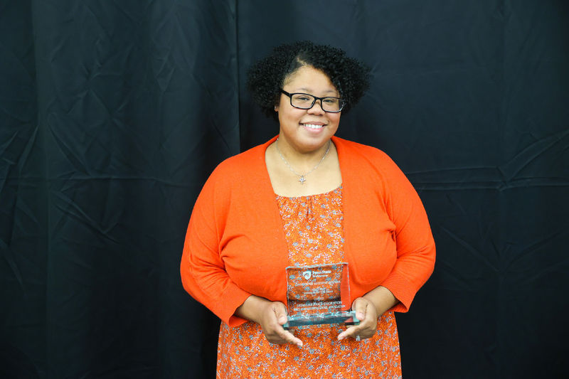 Woman wearing orange smiling in front of a black backdrop