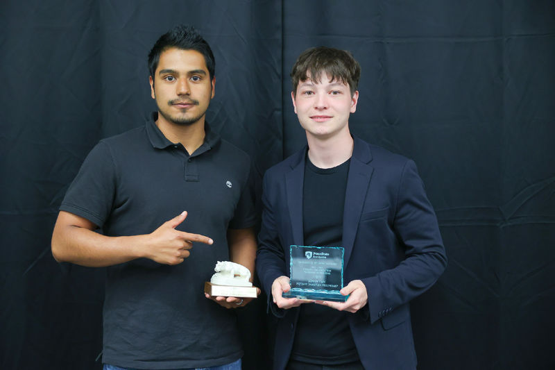 Two men holding awards in front of a black backdrop