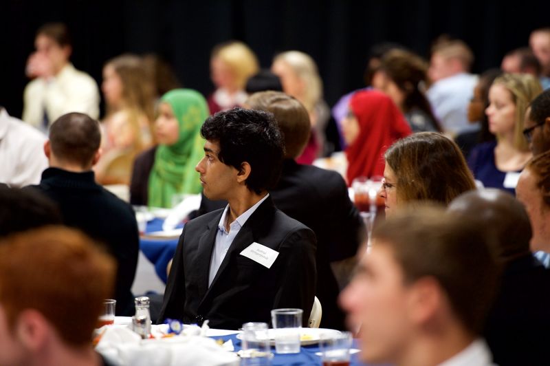 Student sitting at a table listening to a speech.