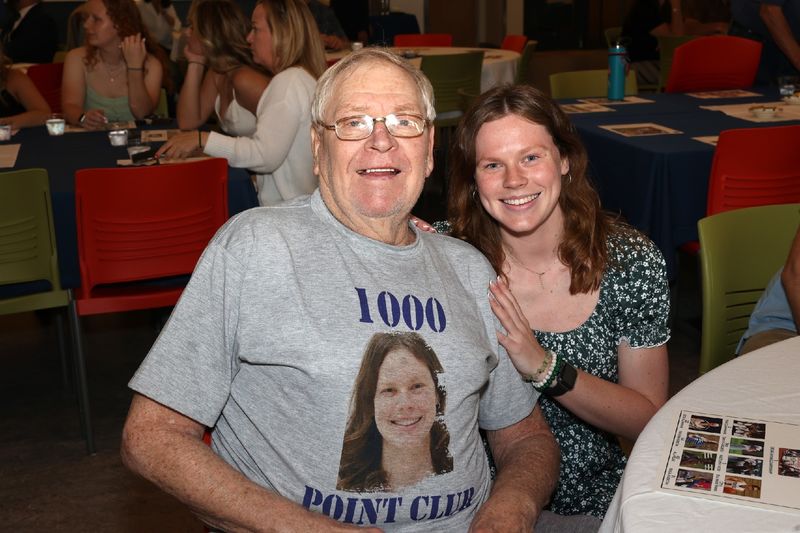a woman and a man sitting next to each other, man wearing shirt that says 1000 points club
