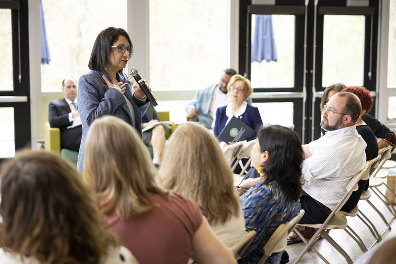 A woman stands and speaks to a group seated.