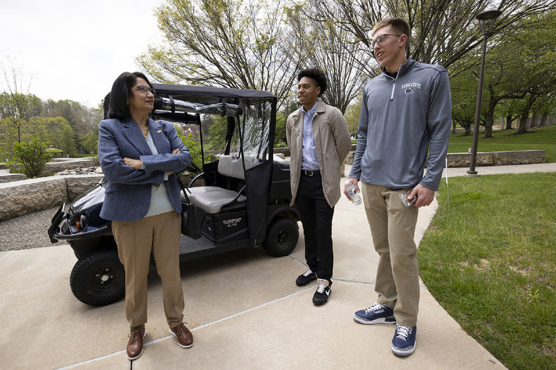 A woman and two men stand next to a golf cart.