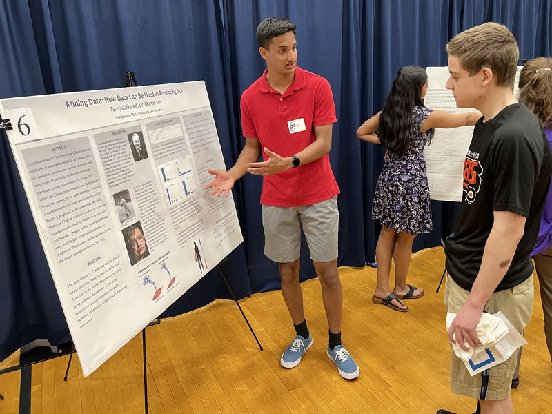 A student points to his poster as another student looks on.
