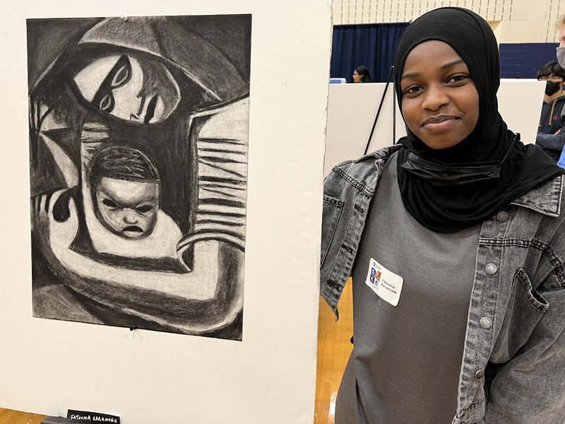 A woman stands next to her artwork.