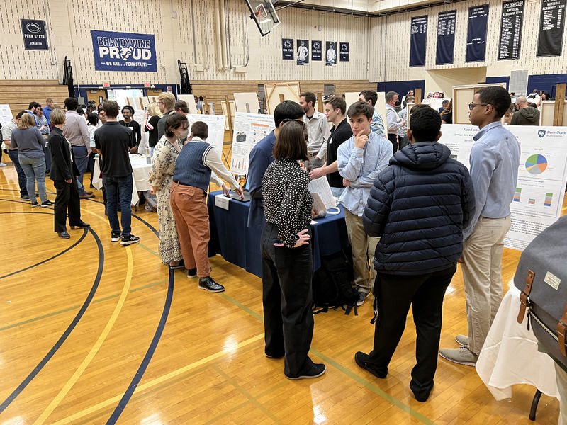 A crowd of people in the campus gym talk with students and look at research posters.