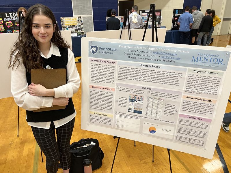 A student stands next to a poster about her internship.