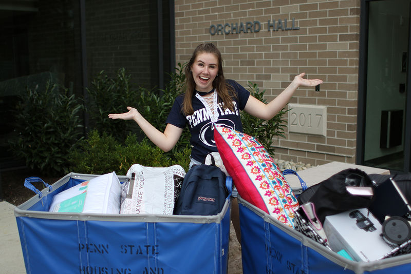 female student standing in front of Orchard Hall with bins to move in