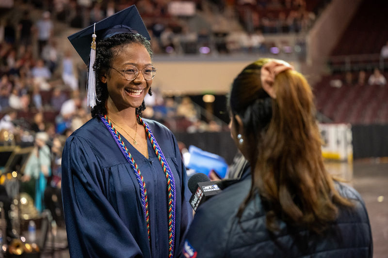 A Penn State Behrend graduate talks with a TV reporter before the college's commencement ceremony.