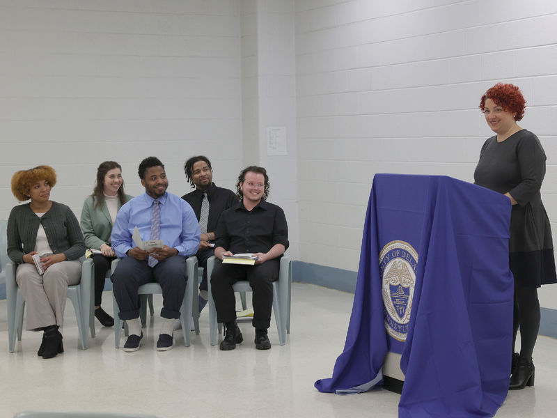 A woman at a lectern speaks to a group of seated people.