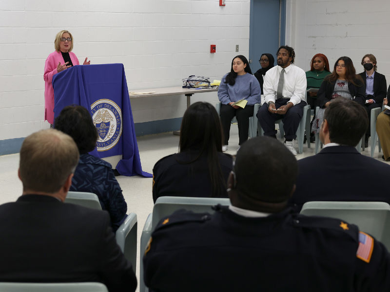 A woman at a lectern speaks to a group of people seated.