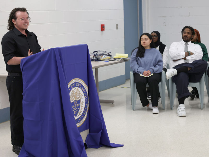 A male student speaks at a lectern to a group of people seated.