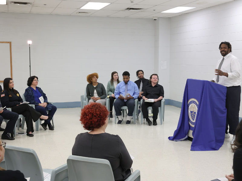 A man stands at a lectern speaking to a group of people seating.