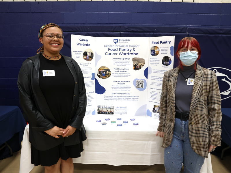 two students standing in front of a poster for the center for social impact