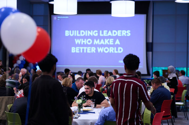 crowd sitting at tables with "building leaders who make a better world" on projector