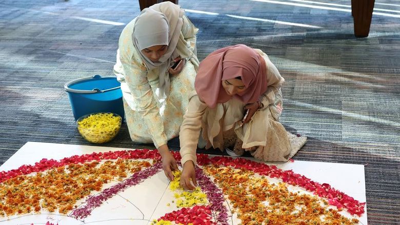 Two female students place flower petals onto the floor to create a rangoli.