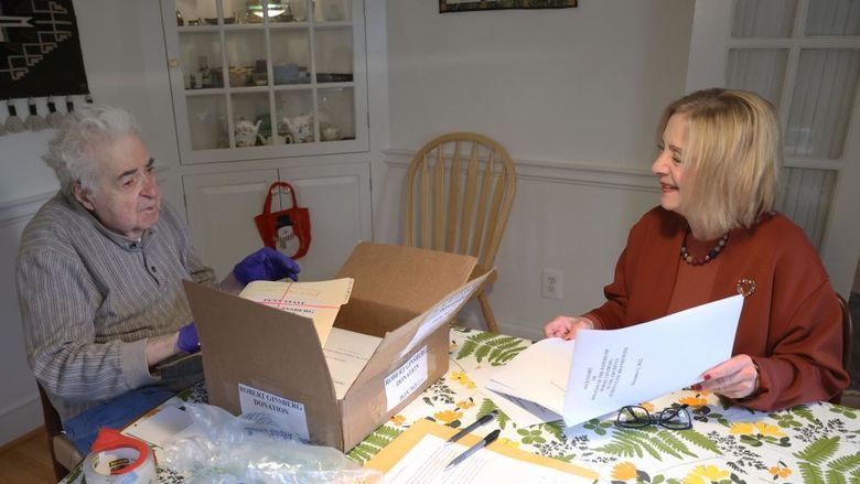 A man and a woman sit at a dining room table look at files.