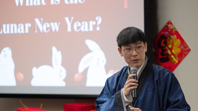 A male student stands at a podium wearing a traditional Chinese robe.