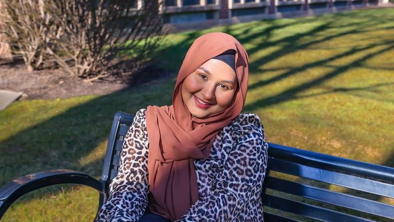 Girl sitting on a bench wearing a cheetah print shirt and pink hijab