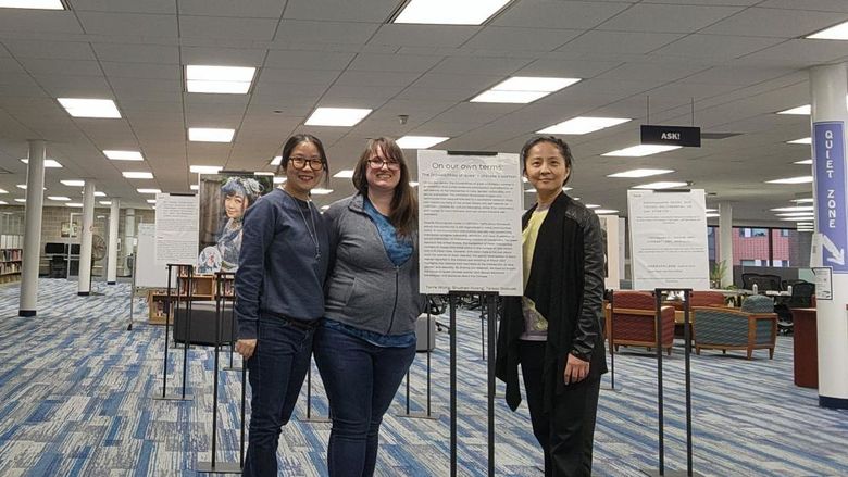 Three women standing in front of sign for exhibit