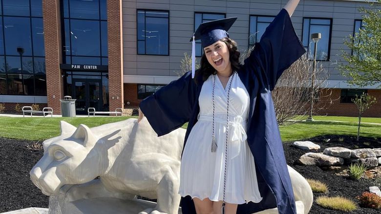 New Penn State graduate Anna Raffeinner celebrates with a joyful expression with the Lion Shrine on the Penn State DuBois campus, just outside the PAW Center