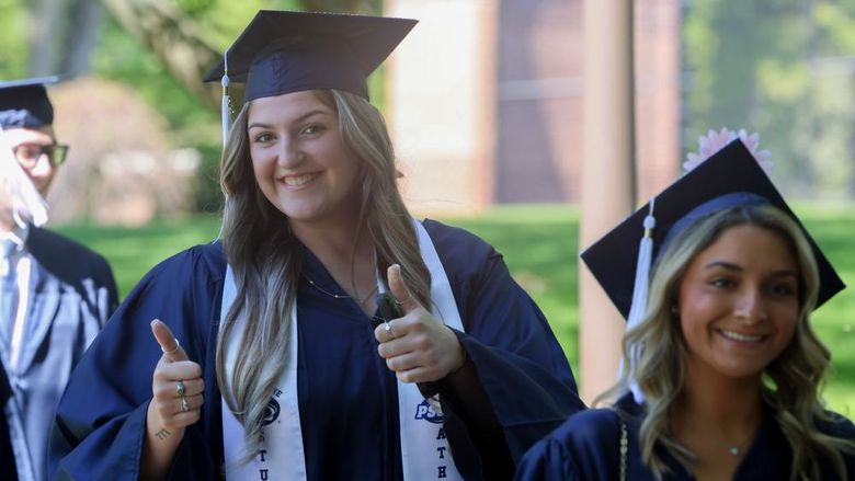 Two women are walking outside wearing commencement caps and gowns.